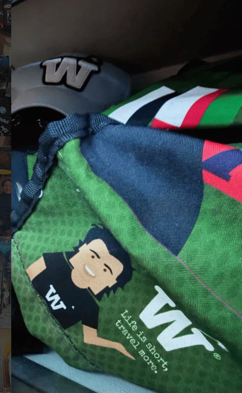 A green WISSHH bag with a cartoon traveler print, packed with other items