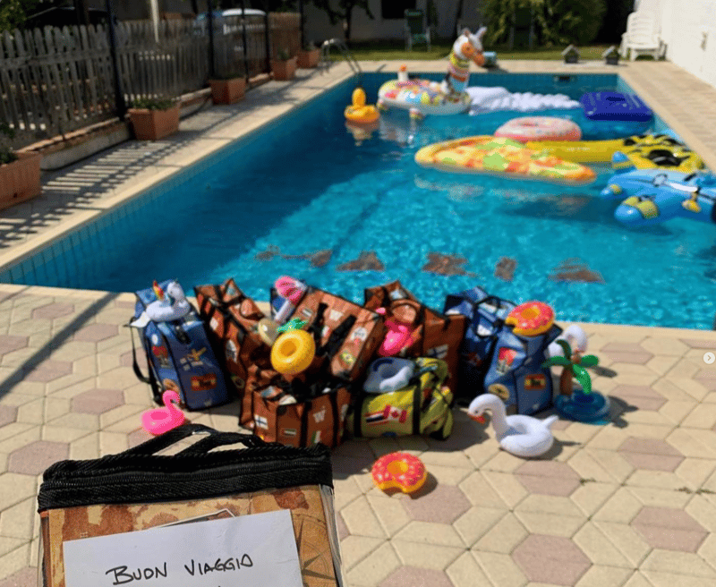 Several WISSHH Travel Bags gathered by a pool next to a handwritten Buon Viaggio sign