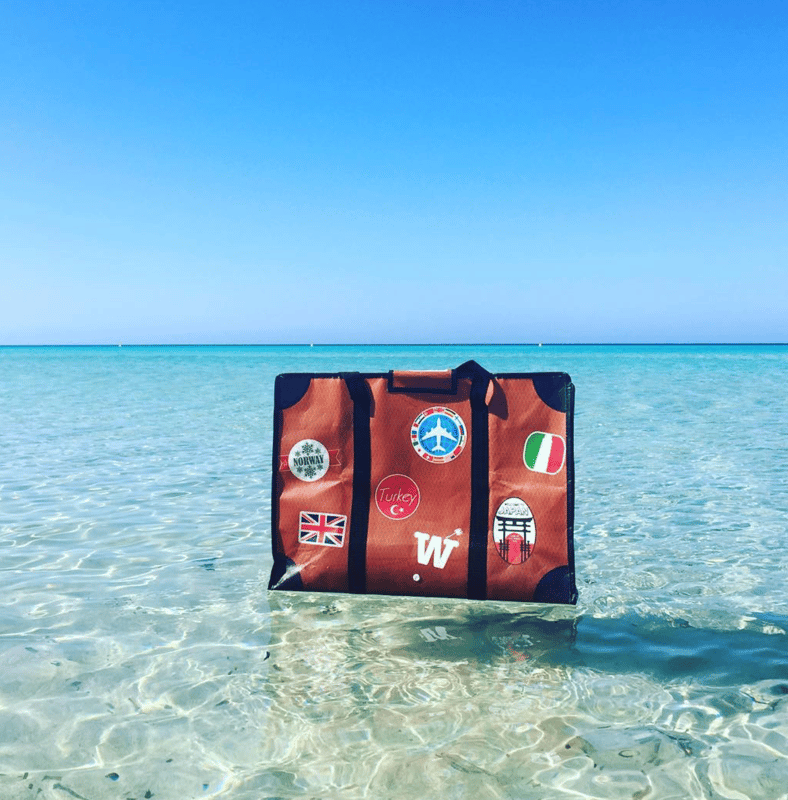 An orange WISSHH Travel Bag floating in a turquoise sea