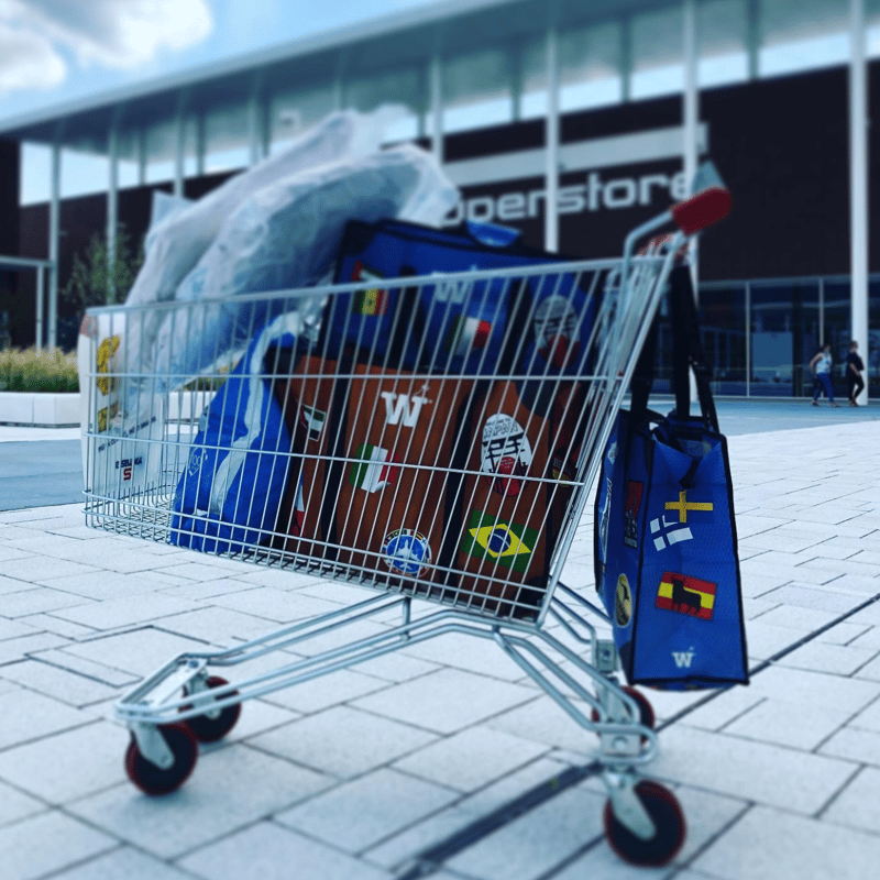 A shopping cart full of groceries with WISSHH bags hanging from the sides, outside a supermarket