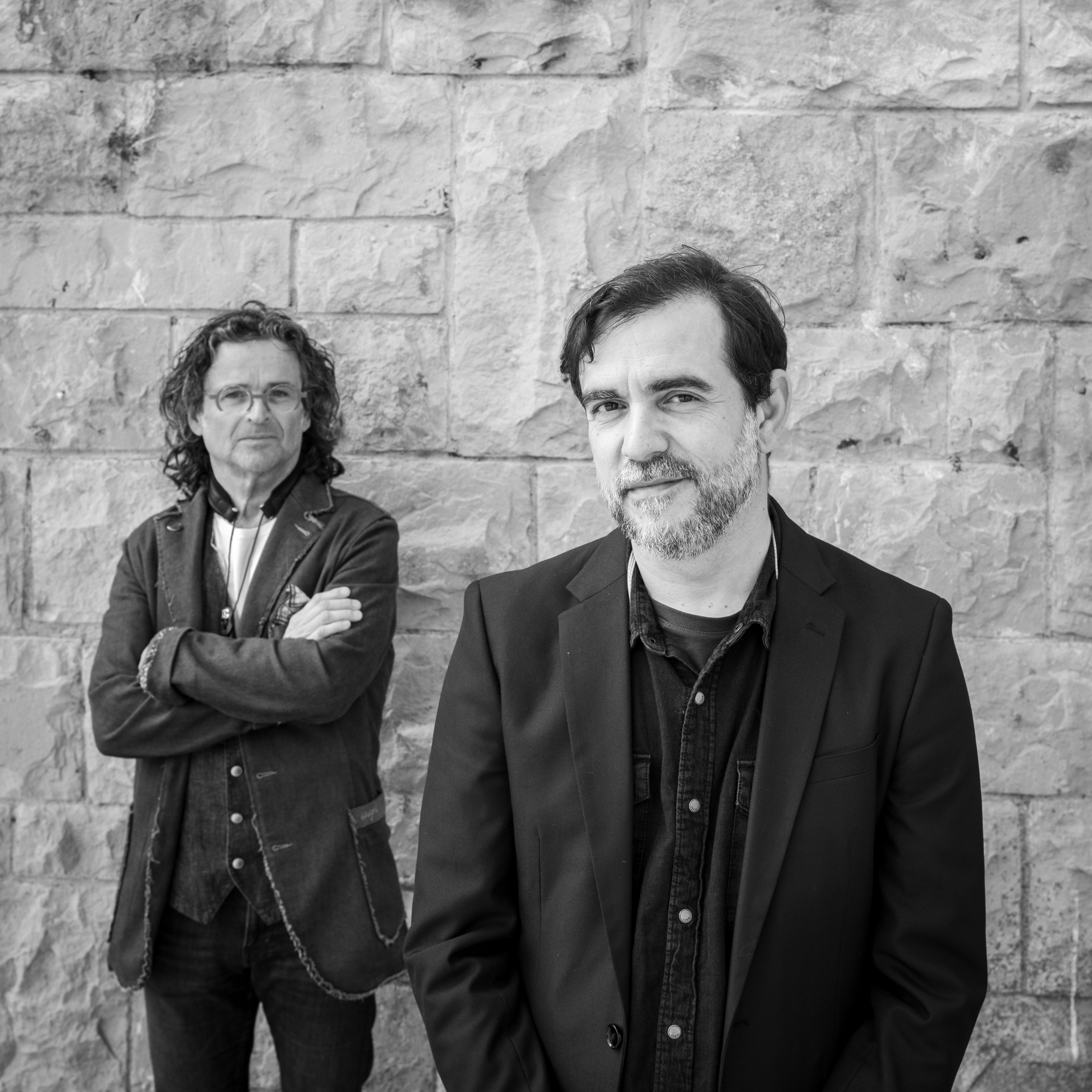Joan Tena y Pep Poblet, fotografiados en blanco y negro delante de una pared de piedra