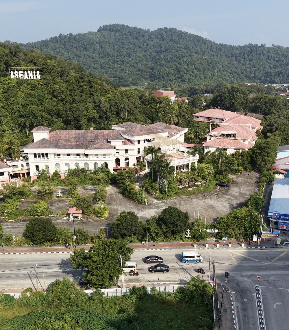 An overgrown, apparently abandoned resort building with a faded ASEANIA sign visible on the forested hillside behind it